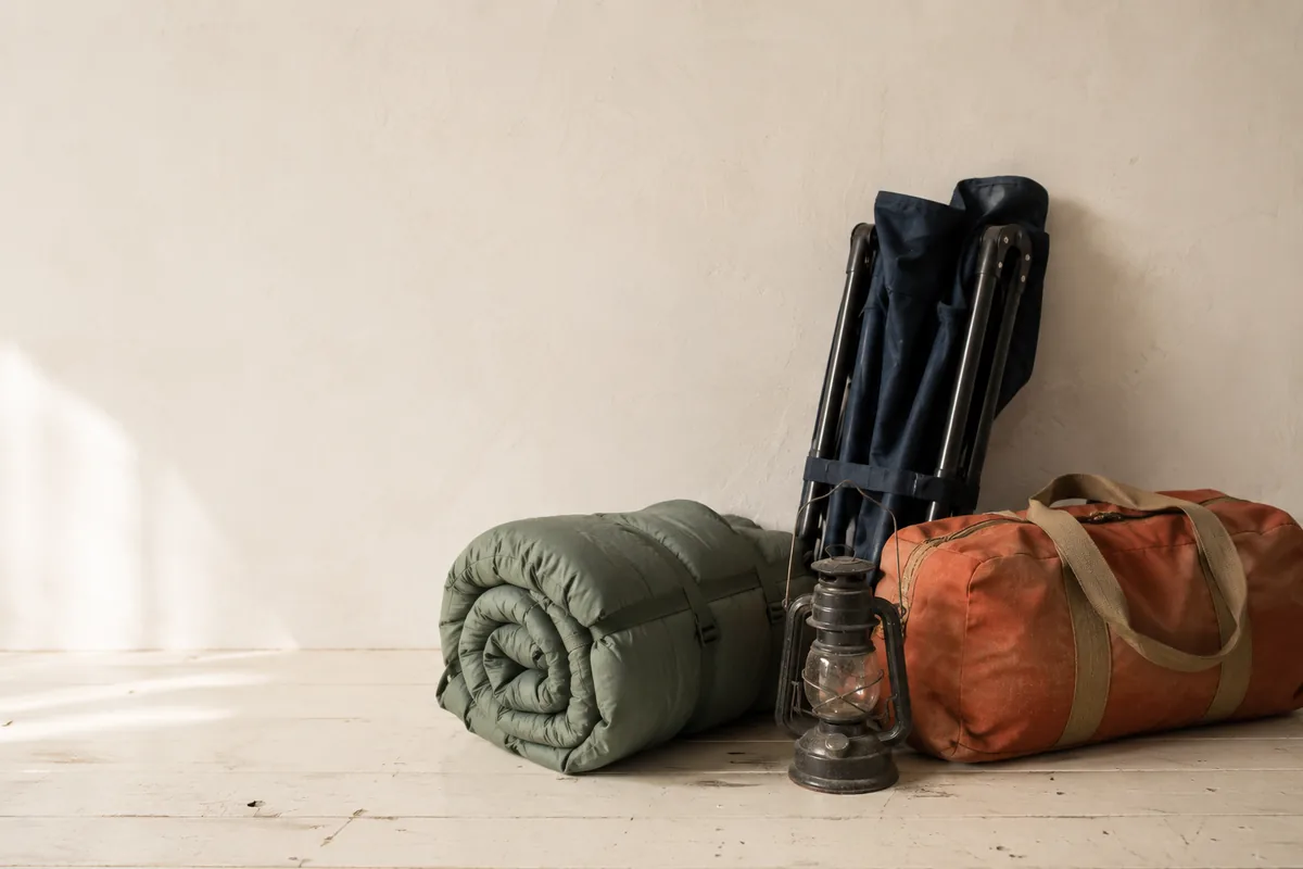 Sleeping bag, folded camp chair, lantern and duffel arranged on the floor.